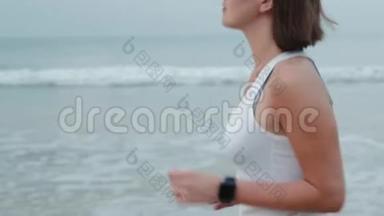 运动女跑步者穿着带<strong>表带</strong>的智能<strong>手表</strong>跑，带空白黑色玻璃弯曲触摸屏的天然海洋海滩